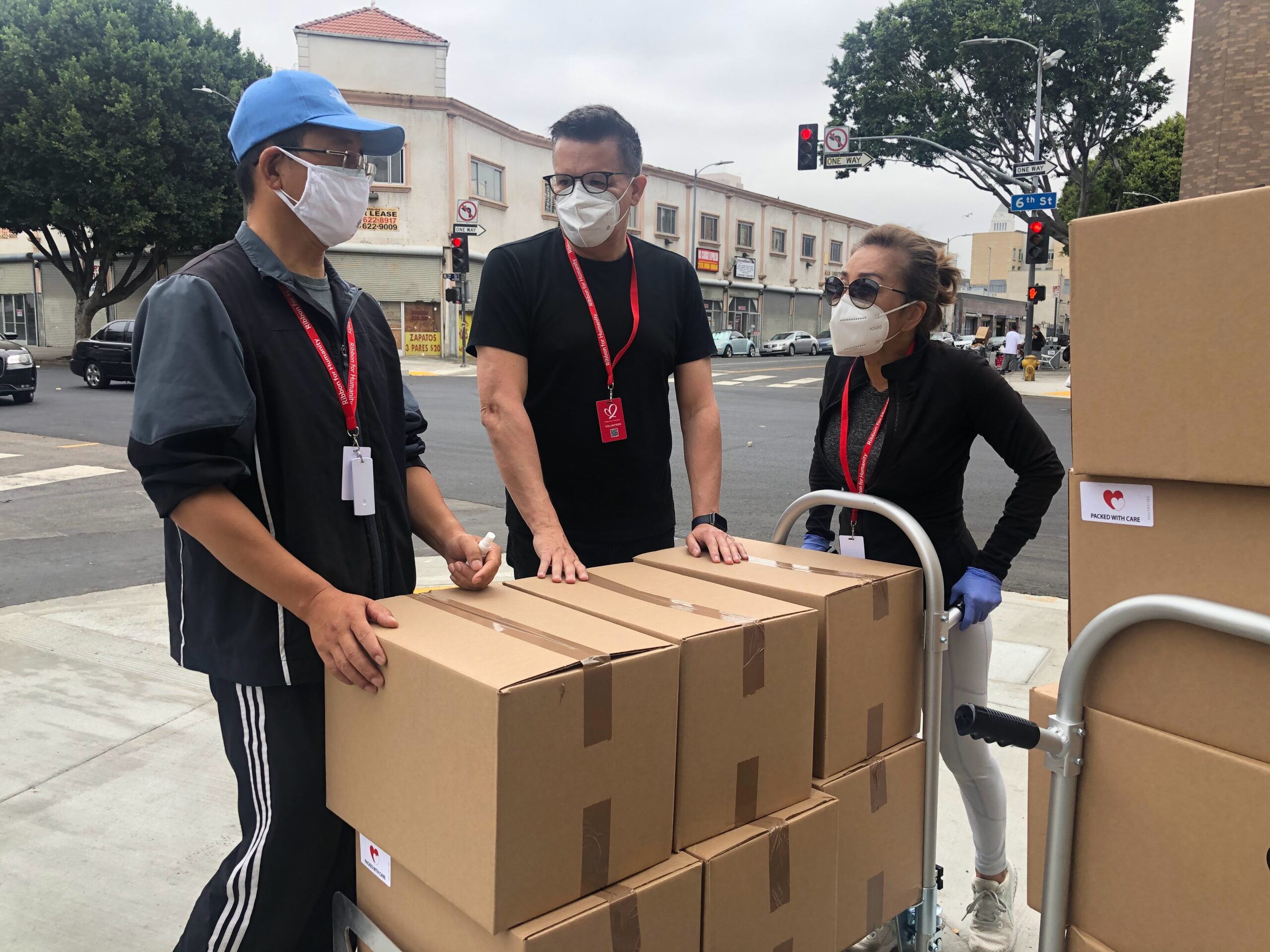 3 people in black shirts standing next to a trolly with boxes.