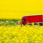 Red truck driving past yellow fields