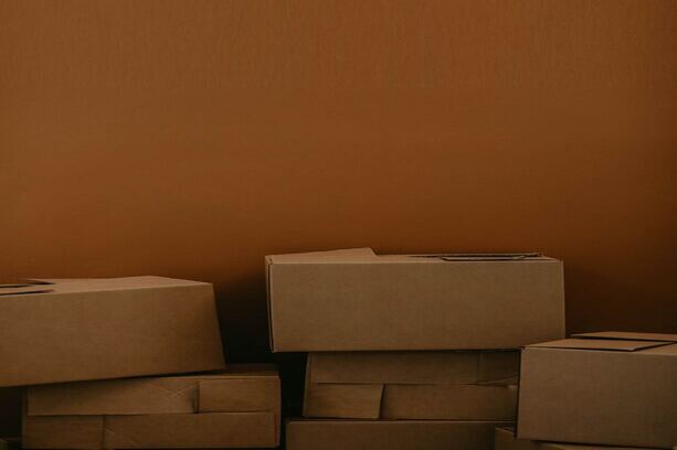 A stack of cardboard boxes placed before a brown wall, forming a neat pile.