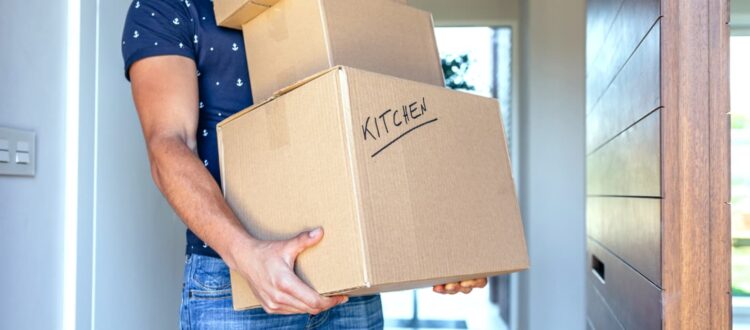A man carries a stack of boxes, one is marked with the word “kitchen”.
